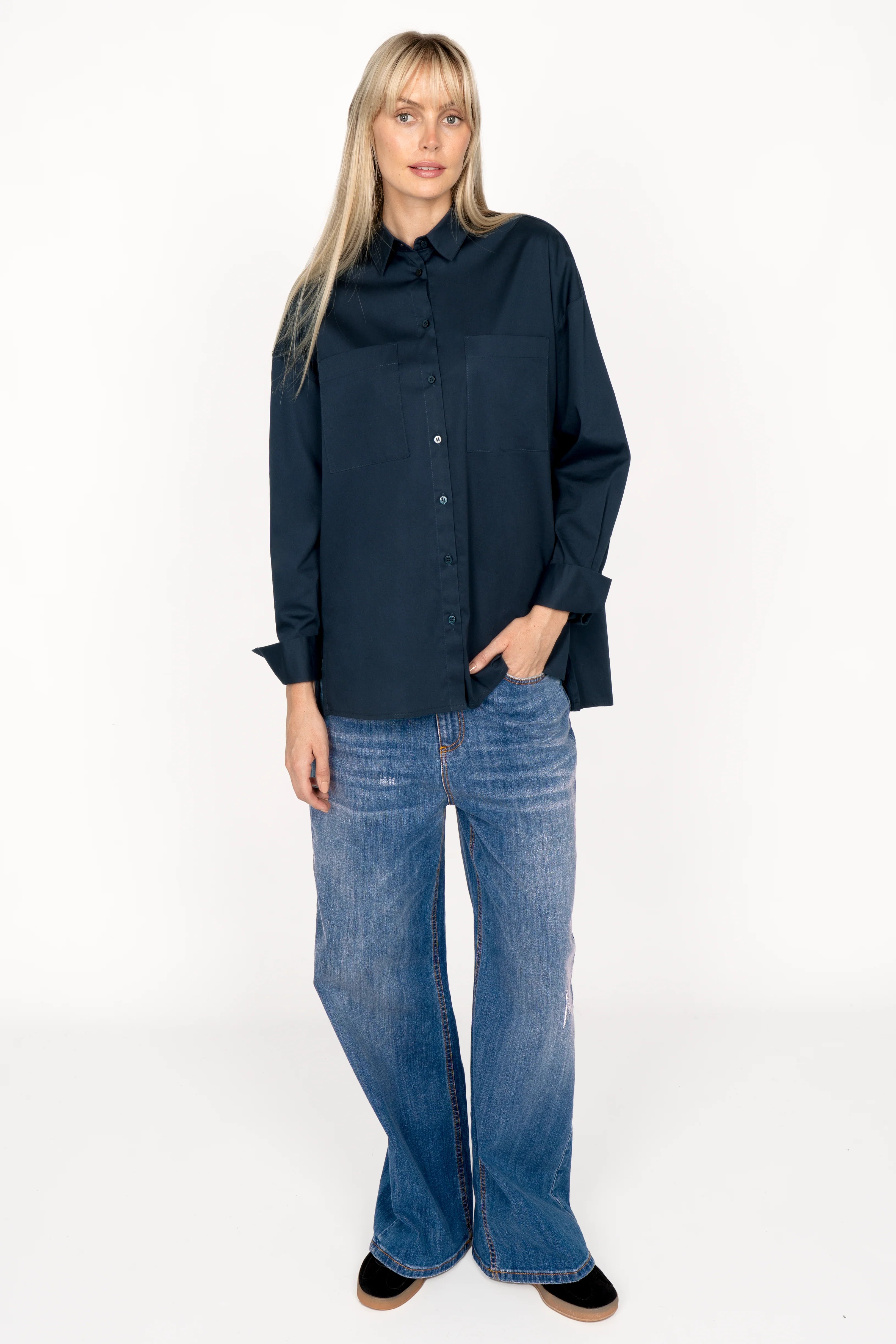 Woman wearing navy blue LEA.K loose fit blouse with button-up front, chest pockets, wide cuffs, and longer back paired with blue jeans