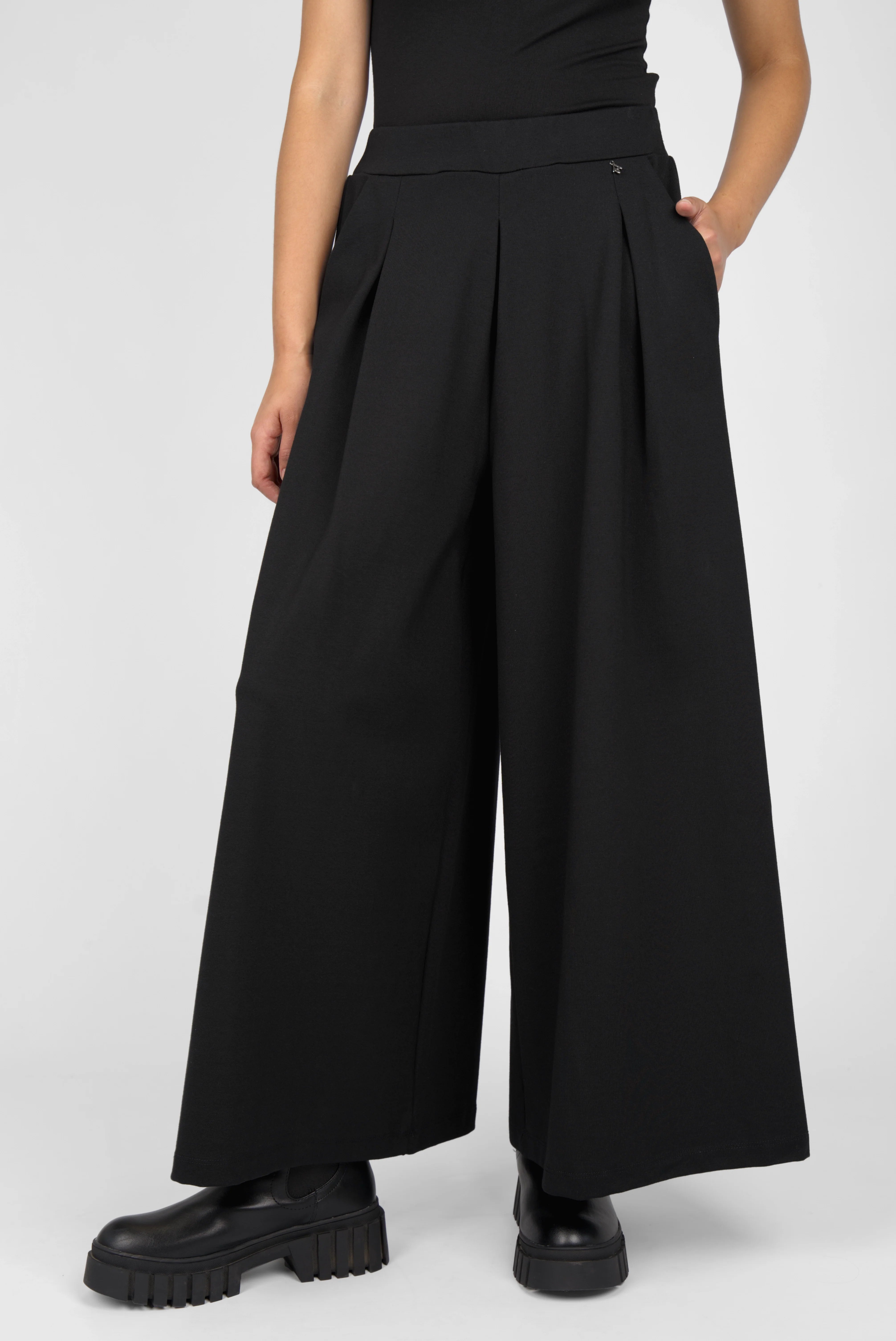Black LINNEE wide-leg pants with front pleats, elastic waistband, and side pockets in relaxed fit.
