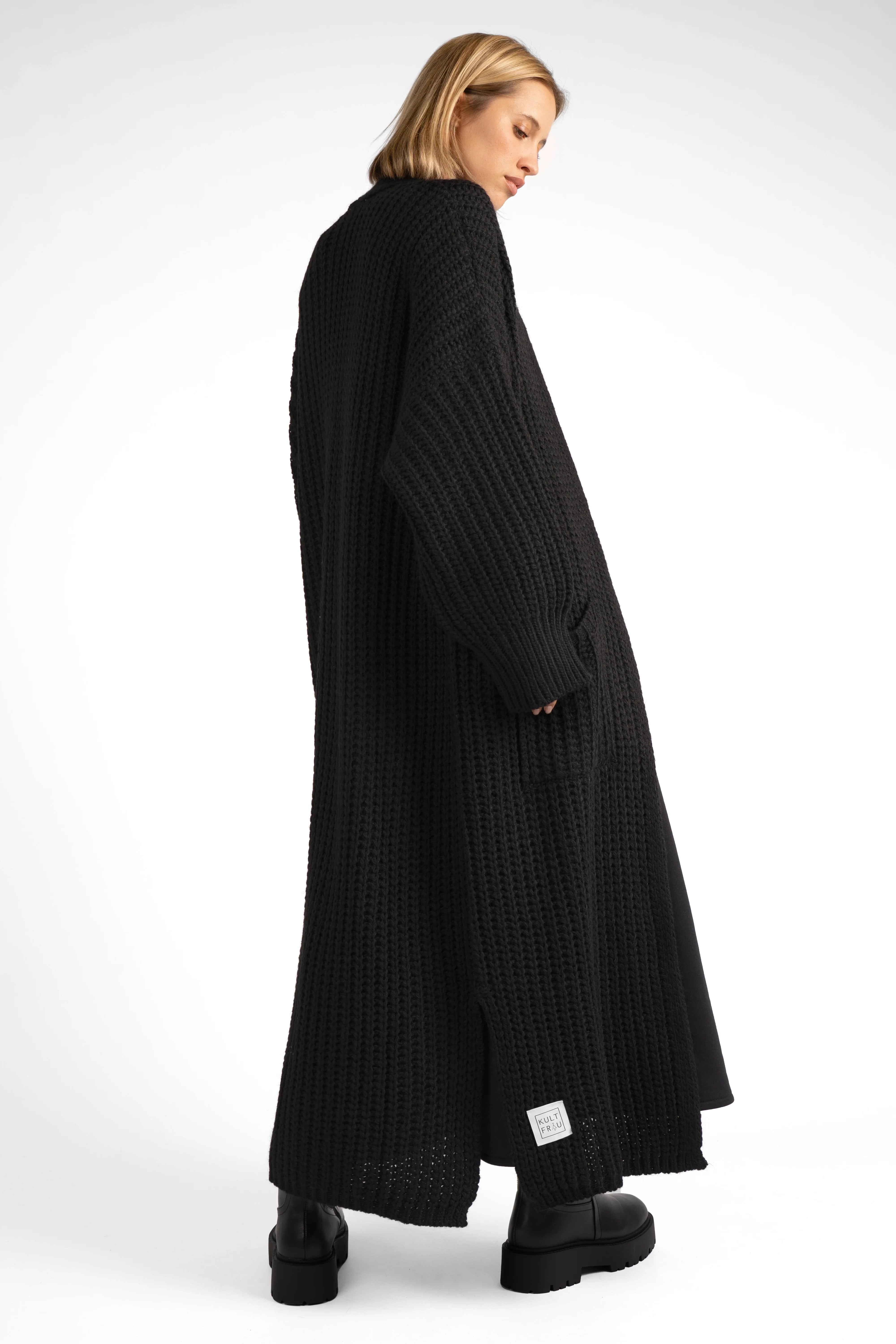 Woman wearing long black oversized LOLA Strickcardigan with relaxed fit and pockets, standing sideways