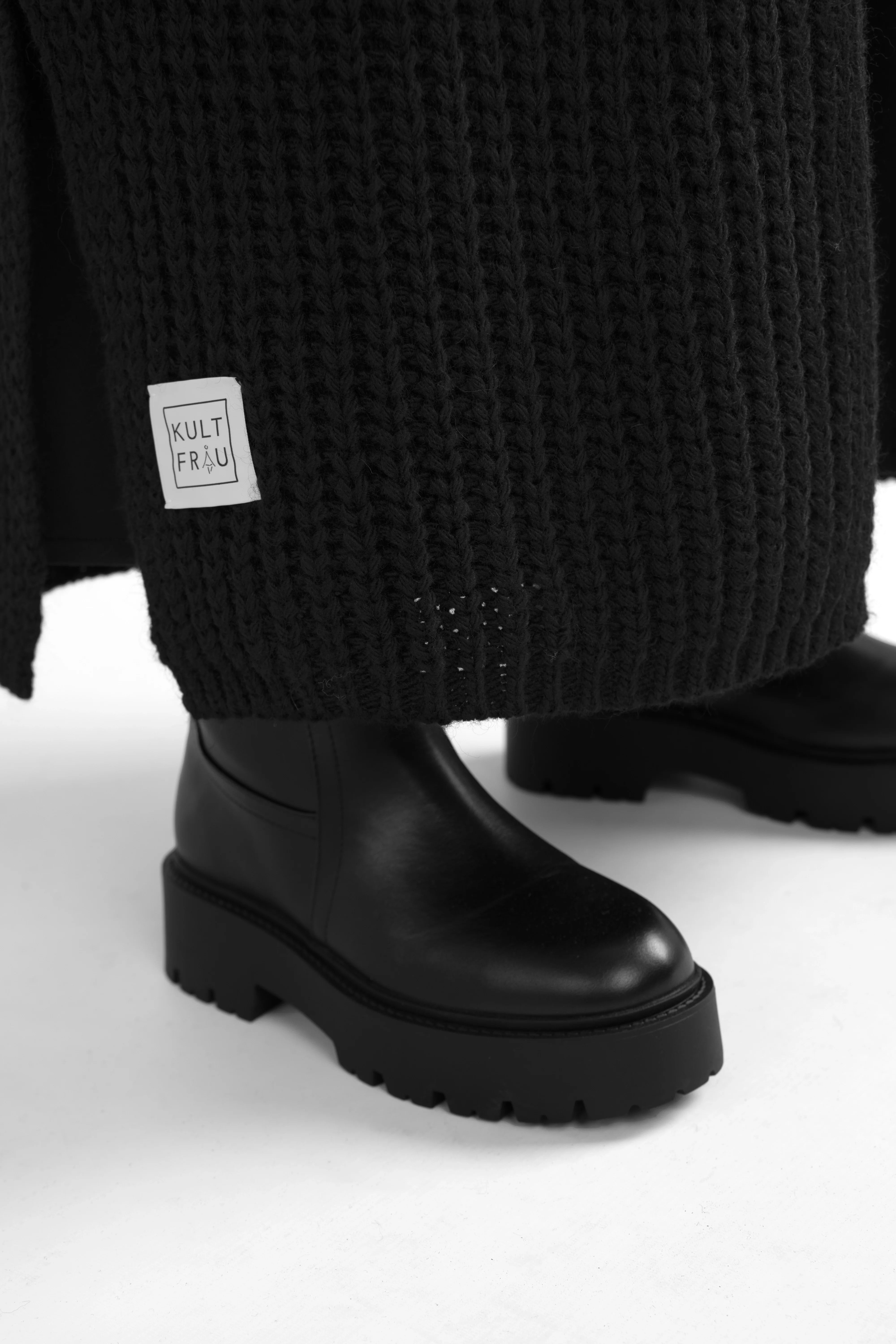 Close-up of black LOLA Strickcardigan knit fabric and hem with label above black chunky sole boots