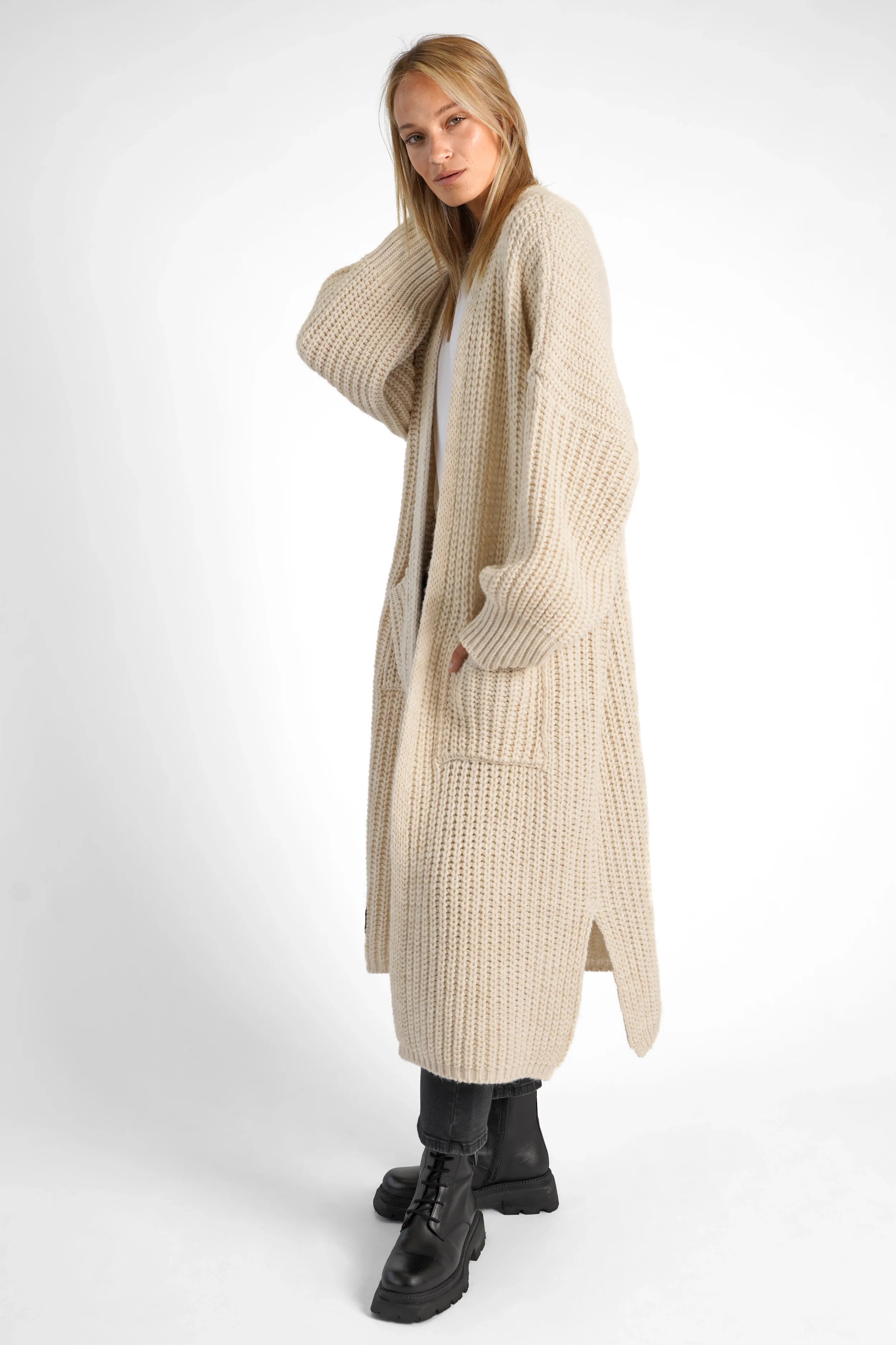 Frau trägt den beigen LOLA Strickcardigan oversize mit aufgesetzten Taschen und locker umgeschlagenen Ärmeln.