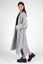 Woman wearing a gray oversized LOLA Strickcardigan with open front and cuffed sleeves, paired with jeans and black boots