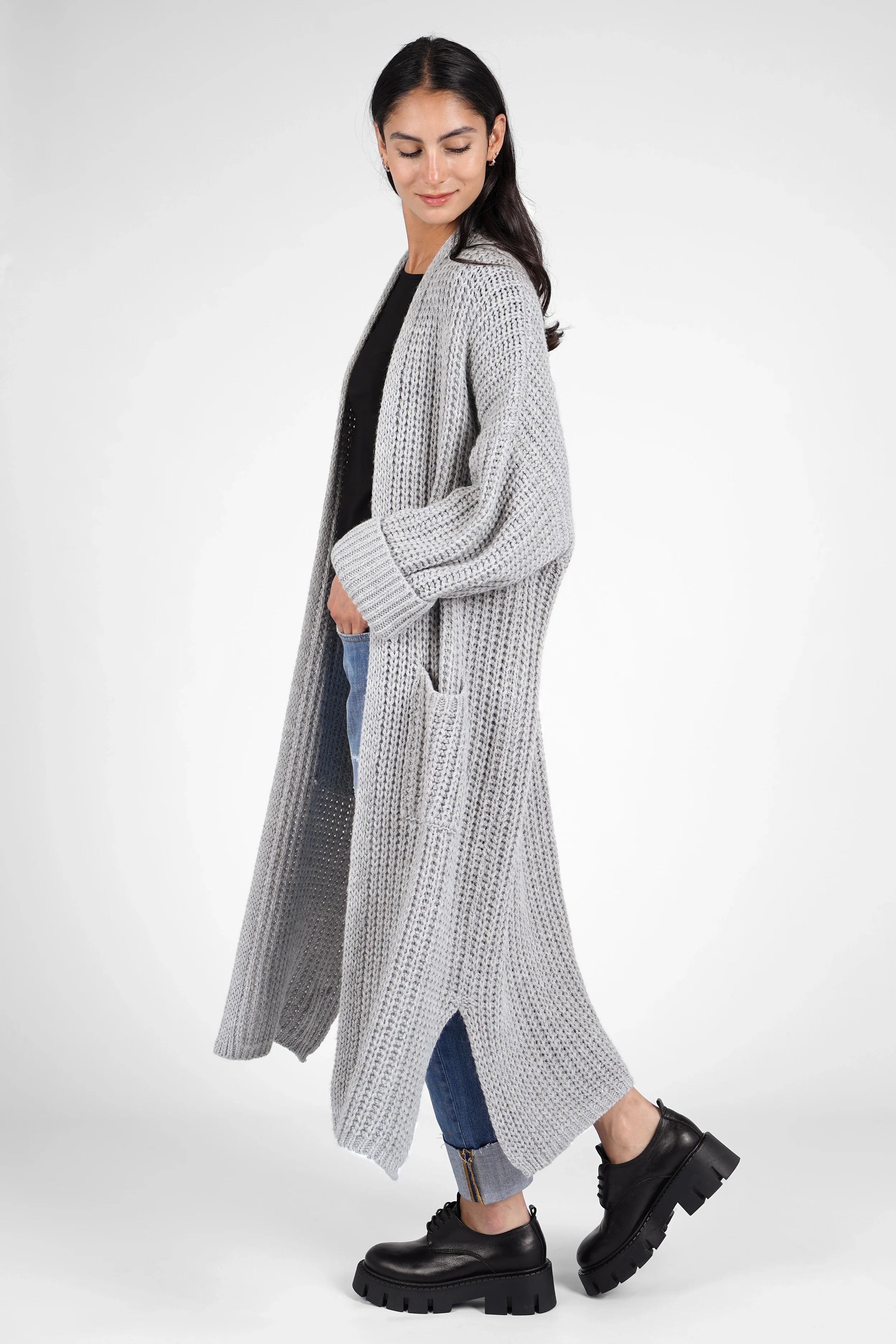 Woman wearing a gray oversized LOLA Strickcardigan with open front and cuffed sleeves, paired with jeans and black boots