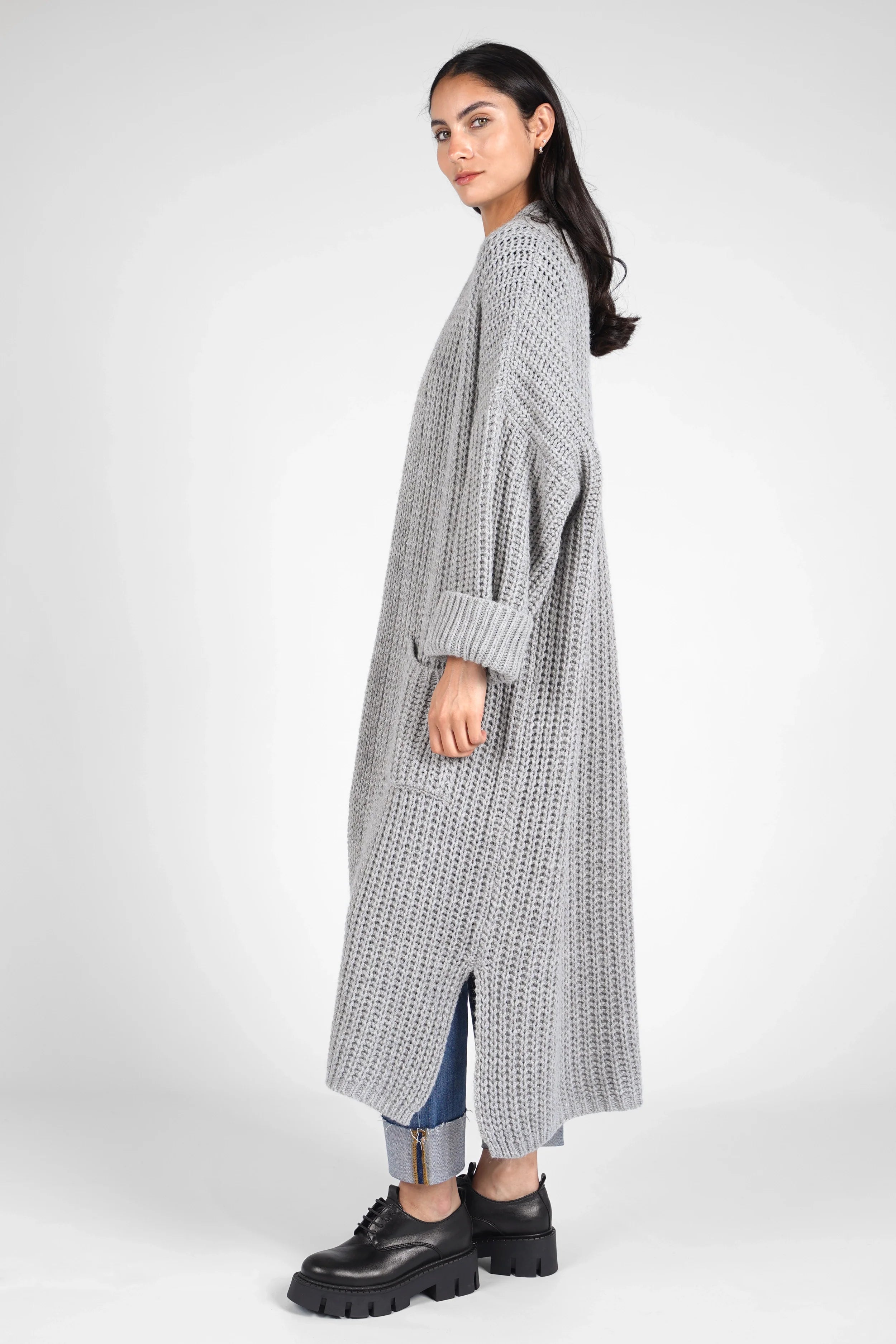 Woman wearing grey oversized LOLA Strickcardigan knit cardigan with rolled sleeves and side slits, styled with jeans and black shoes.