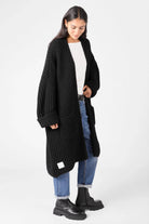 Frau trägt schwarzen LOLLYTA Strickcardigan oversized offen mit aufgesetzten Taschen und umgeschlagenen Ärmeln