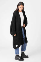 Damen trägt schwarzen oversized LOLLYTA Strickcardigan mit offenen Fronttaschen und umgeschlagenen Ärmeln kombiniert zu Jeans und Boots