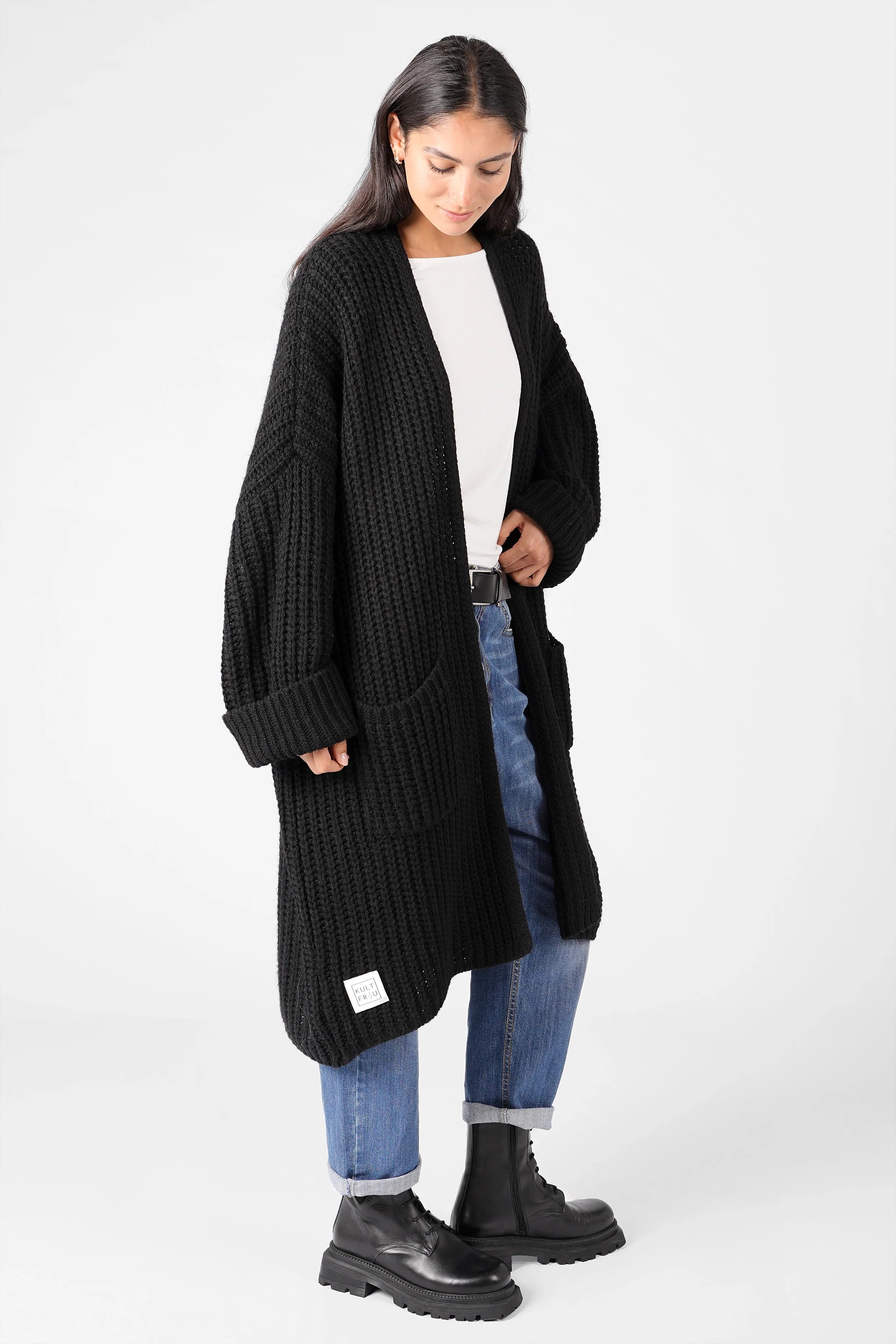 Damen trägt schwarzen oversized LOLLYTA Strickcardigan mit offenen Fronttaschen und umgeschlagenen Ärmeln kombiniert zu Jeans und Boots
