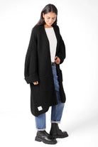 Woman wearing black LOLLYTA Strickcardigan oversized knit with rolled sleeves and front pockets over white top and blue jeans