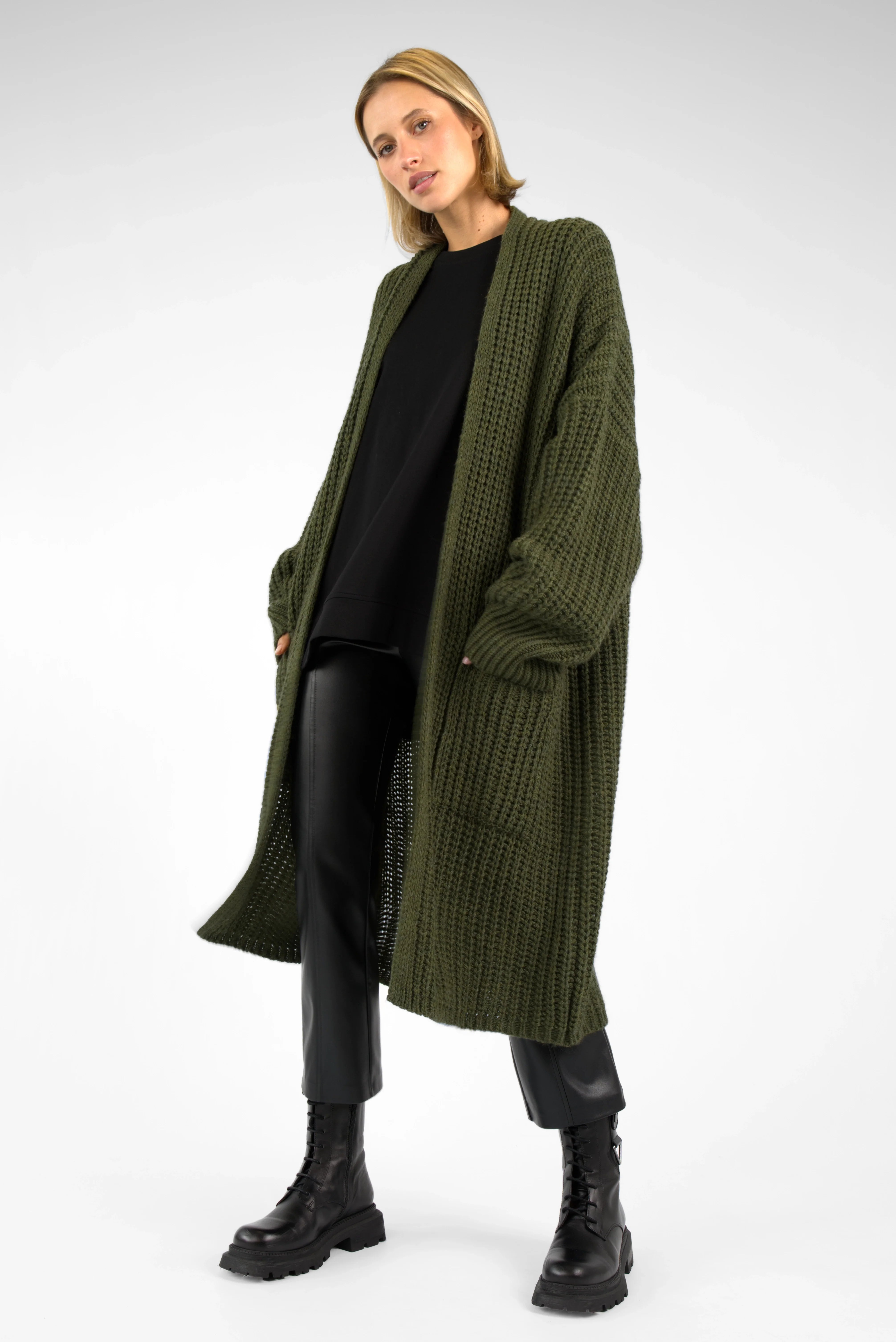Woman wearing oversized olive green LOLLYTA Strickcardigan with open front, relaxed fit, and long sleeves over black outfit and boots