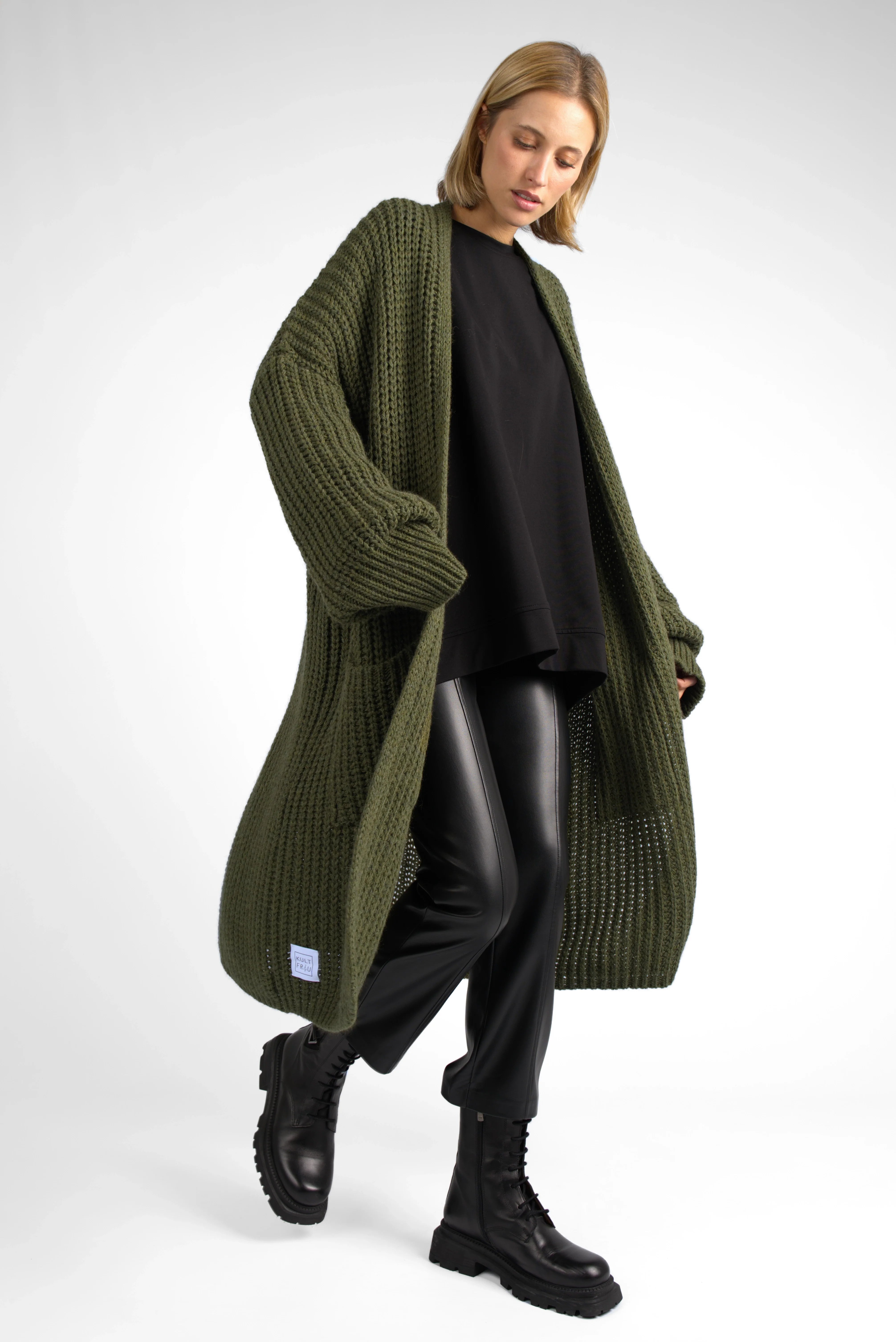 Woman wearing oversized olive green LOLLYTA Strickcardigan with chunky knit, black top, leather pants, and black boots
