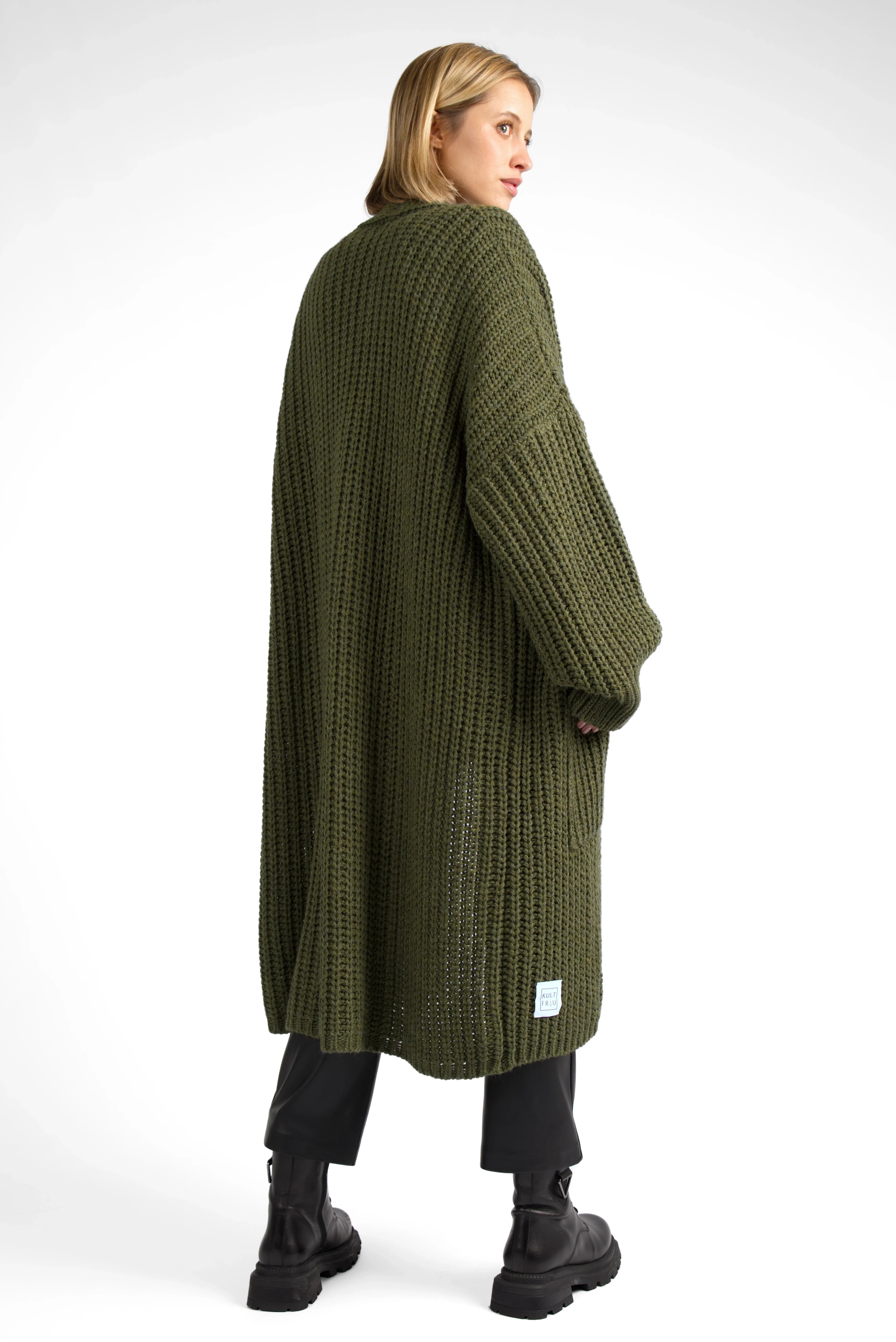 Woman wearing oversized olive green LOLLYTA Strickcardigan with relaxed fit and dropped shoulders, paired with black pants and boots, back view.