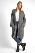 Woman wearing a grey oversized LOLLYTA Strickcardigan with dropped shoulders, patch pockets, and relaxed fit over white top and jeans.