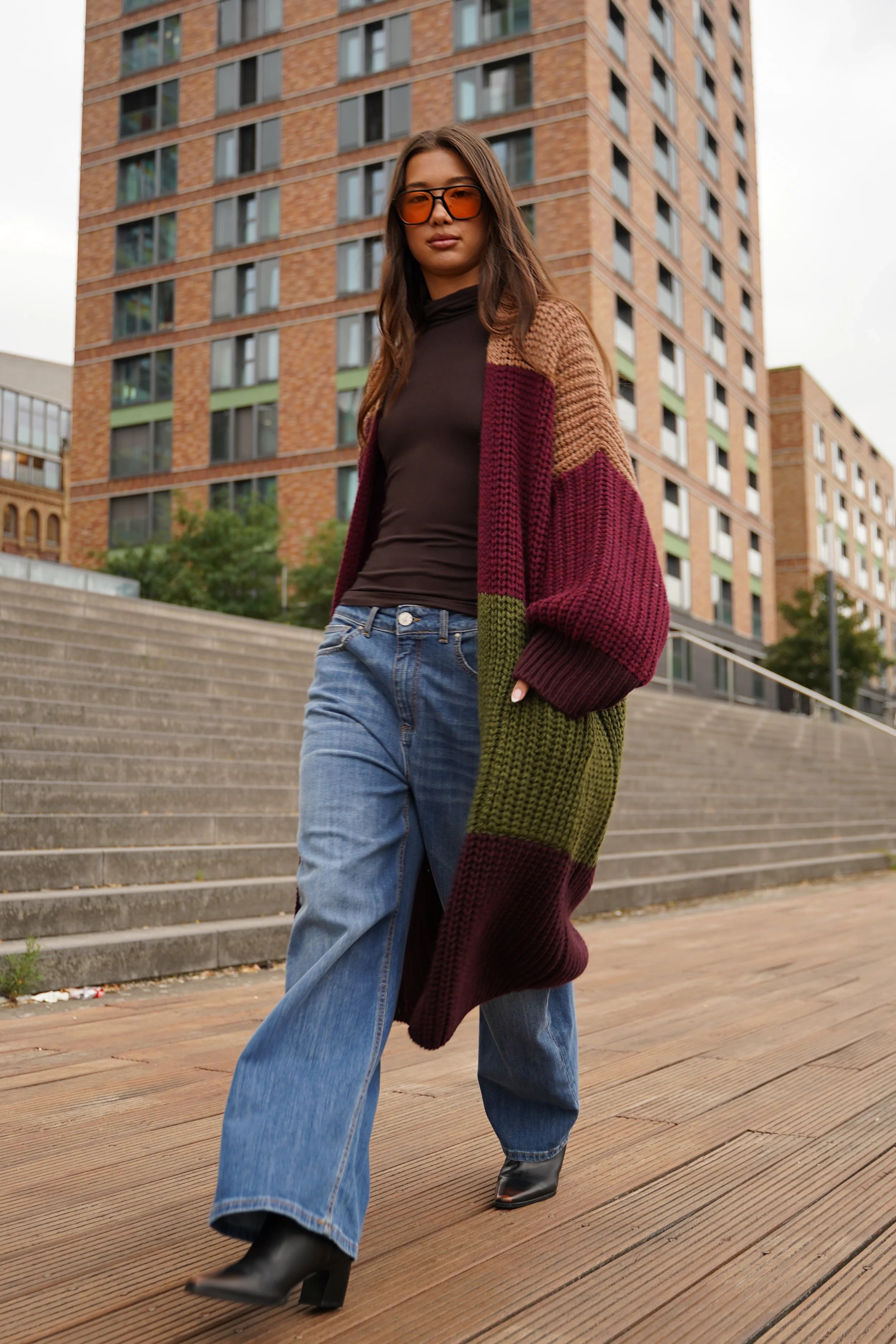 Frau trägt oversized LOLLYTA Strickcardigan in Braun, Bordeaux und Grün mit lässiger Jeans und Stiefeletten draußen