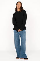 Woman wearing black MALVEA Sweater with relaxed fit and blue jeans