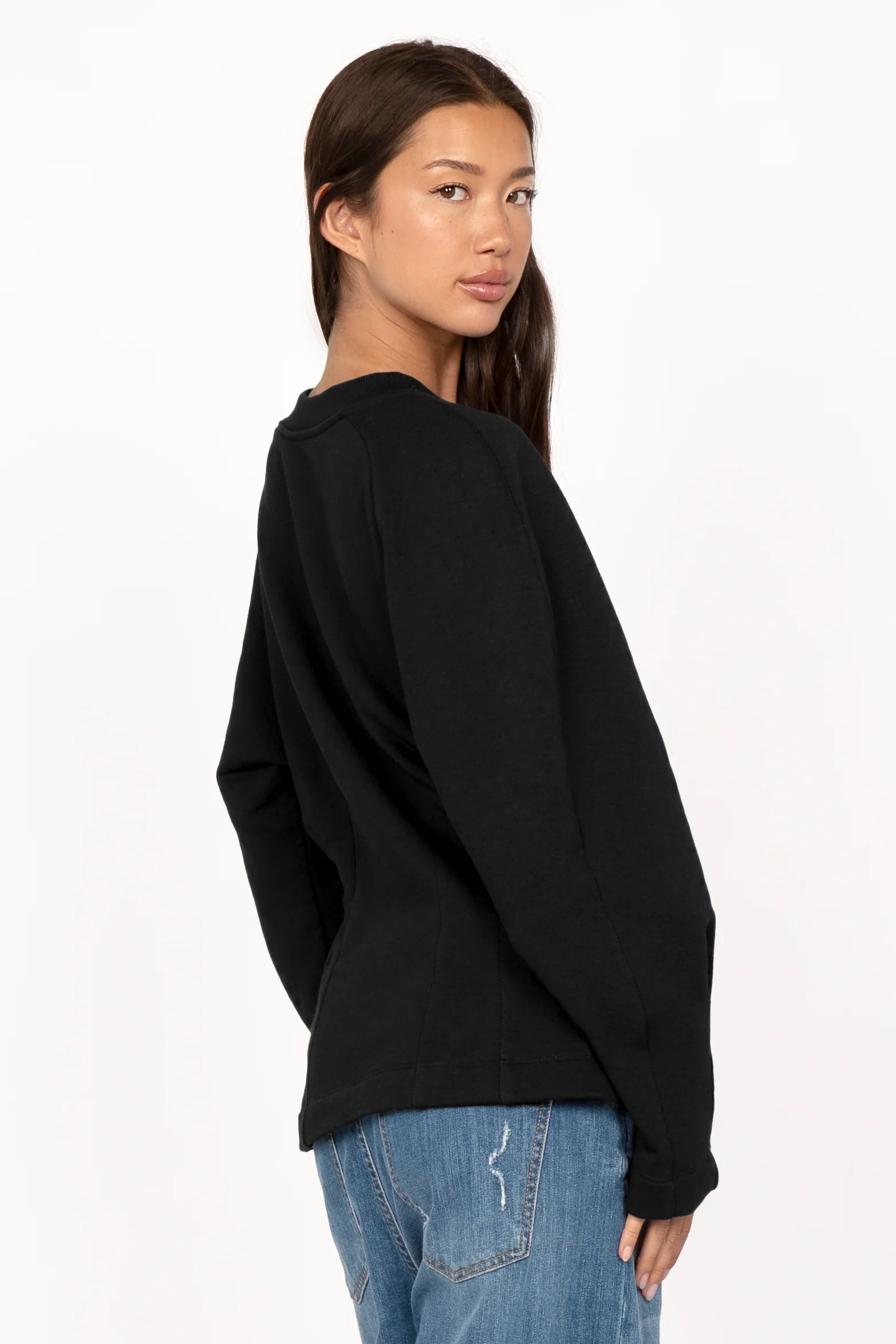 Woman wearing a black MALVEA Sweater with relaxed fit and detailed seam lines on back, paired with blue jeans.