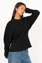 Black MALVEA Sweater with relaxed fit, round neckline, and subtle seam details on a model wearing blue jeans.