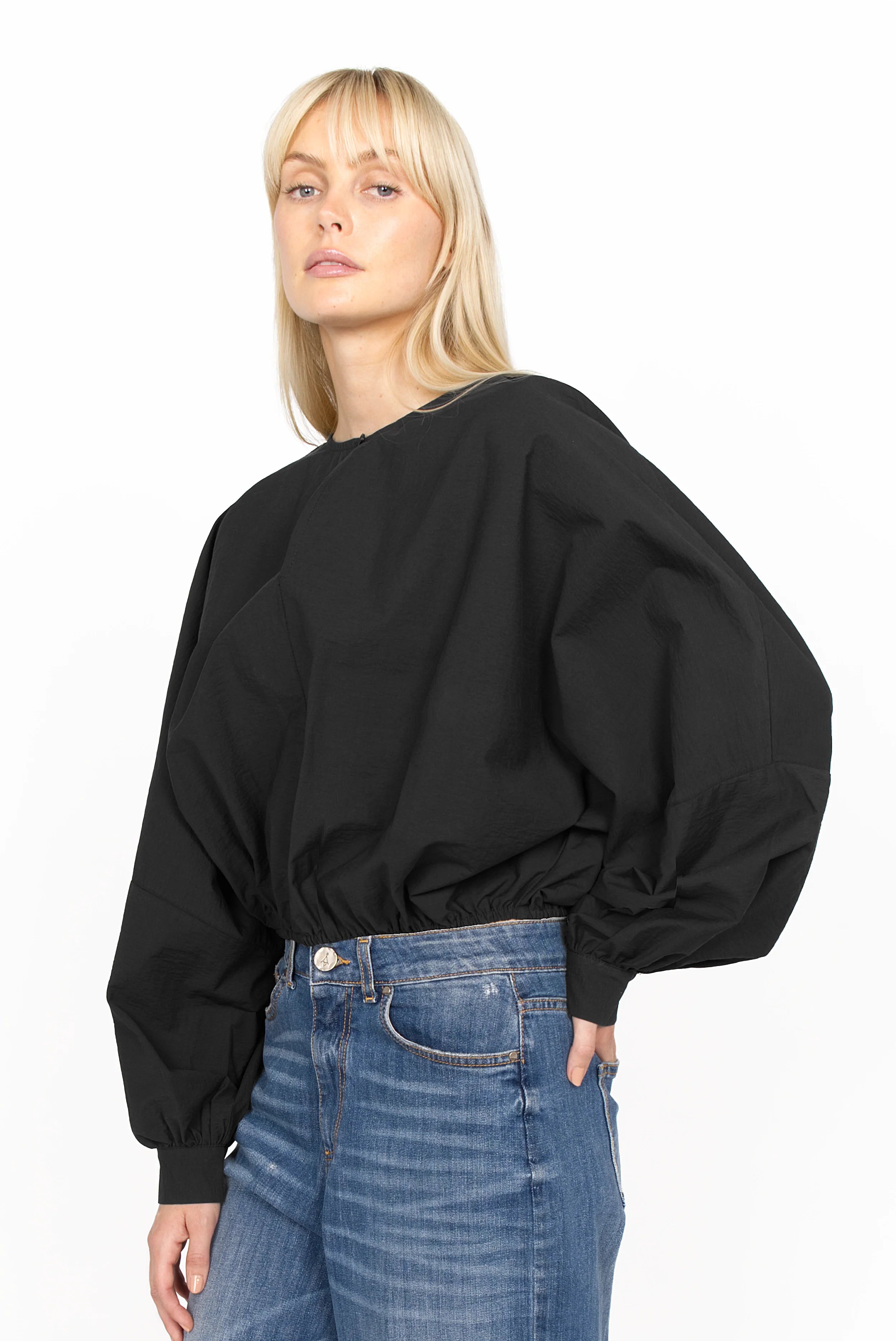Woman wearing black MILLIE Crinkle Bluse with sculptural balloon sleeves and elastic waistband paired with blue jeans