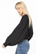 Black MILLIE Crinkle Bluse with balloon sleeves and elastic hem worn with blue jeans, side profile view.