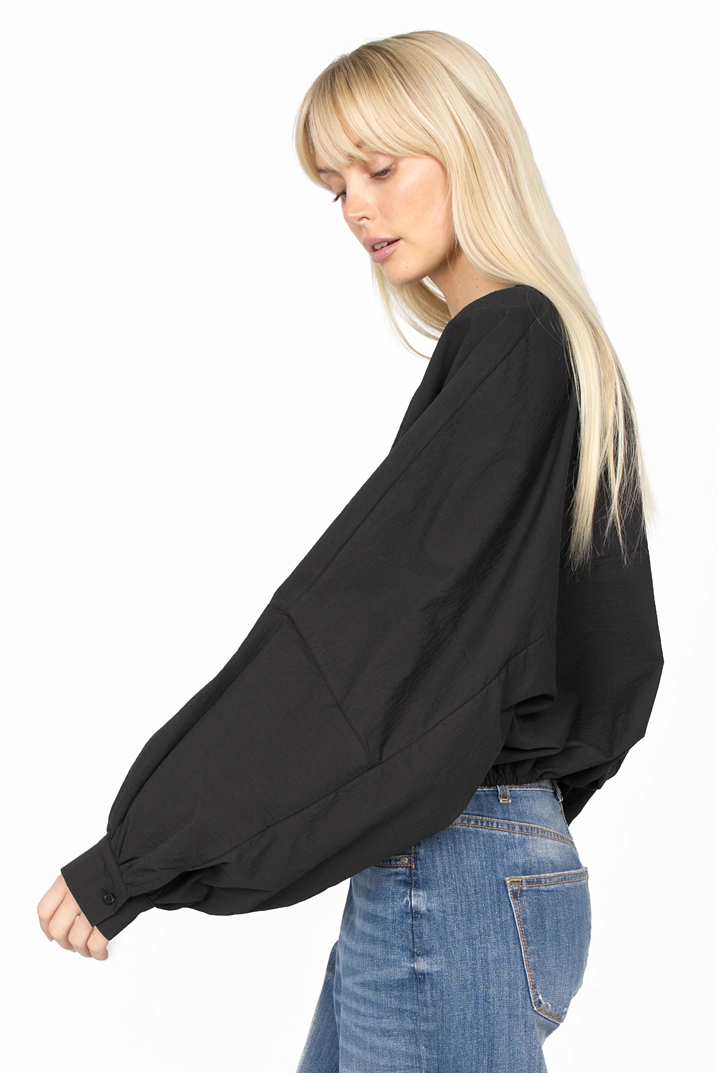 Black MILLIE Crinkle Bluse with balloon sleeves and elastic hem worn with blue jeans, side profile view.