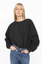 Black MILLIE Crinkle Bluse with sculptural balloon sleeves, elastic hem, cropped loose fit and pearl button neckline detail worn with blue jeans