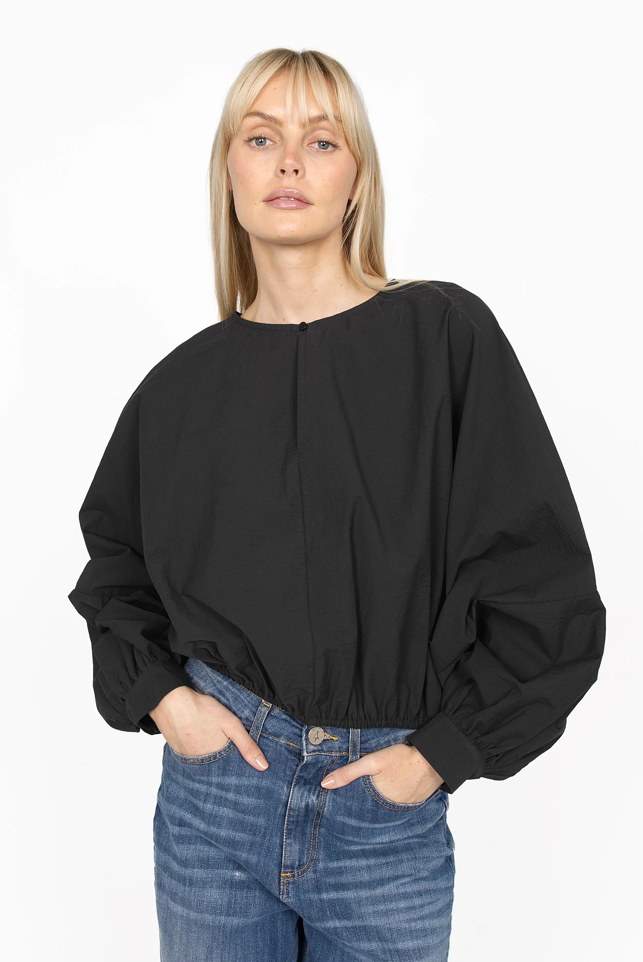 Black MILLIE Crinkle Bluse with sculptural balloon sleeves, elastic hem, cropped loose fit and pearl button neckline detail worn with blue jeans