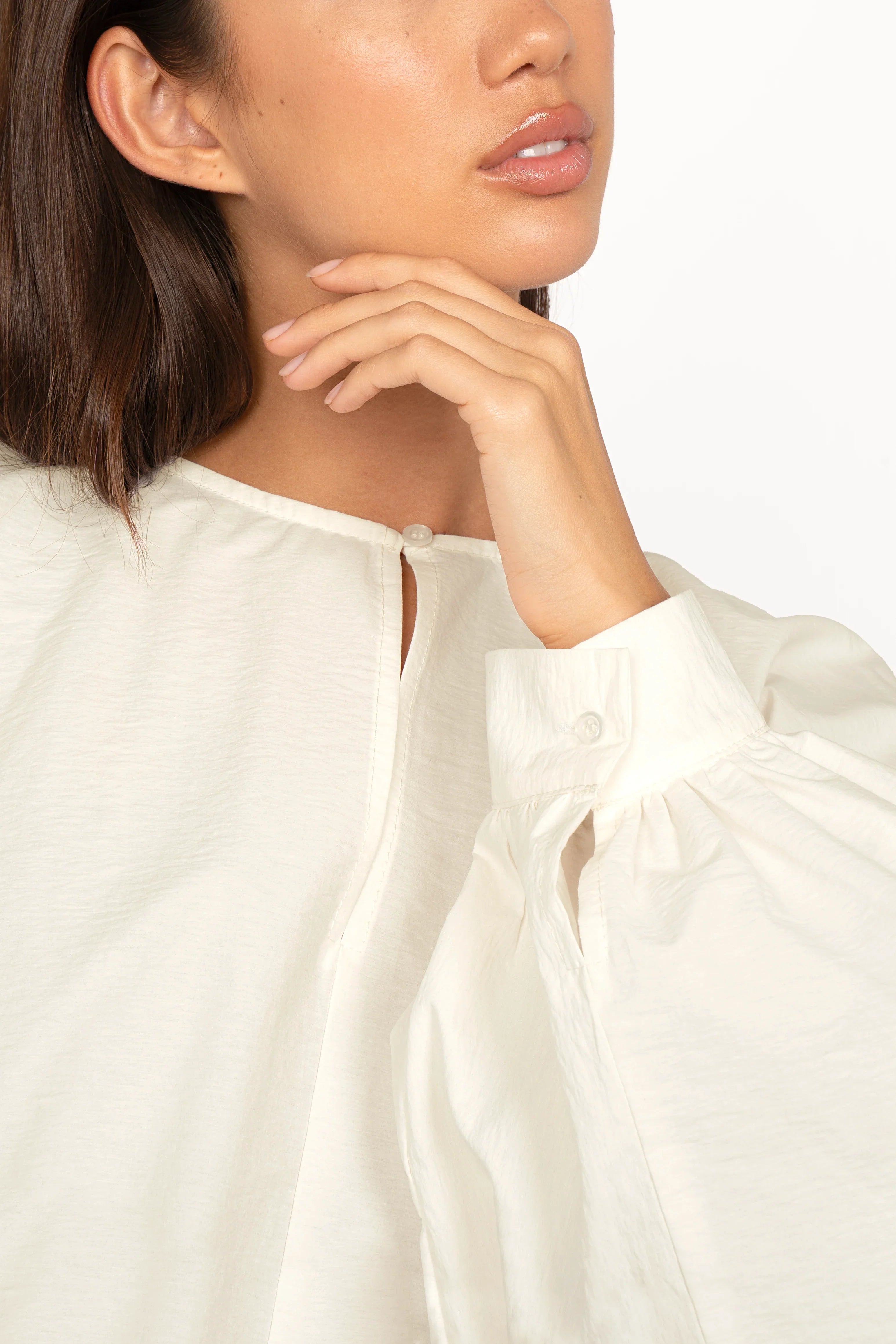 Close-up of woman wearing white MILLIE Crinkle Bluse with balloon sleeves, pearl button at neckline, and buttoned cuffs.