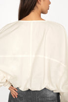 Back view of a woman wearing a loose fit MILLIE Crinkle Bluse with balloon sleeves and elastic waistband in off-white color.