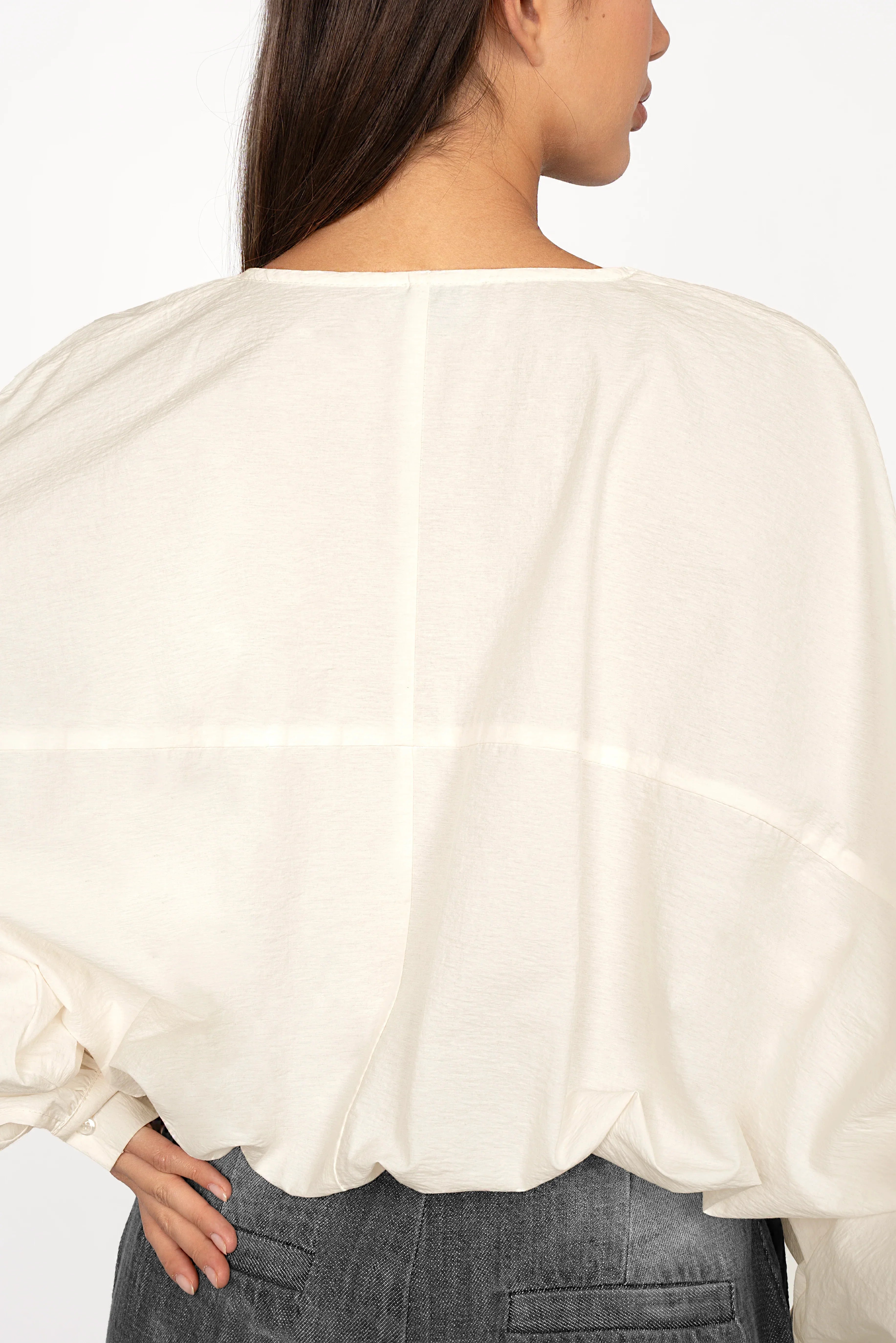 Back view of a woman wearing a loose fit MILLIE Crinkle Bluse with balloon sleeves and elastic waistband in off-white color.