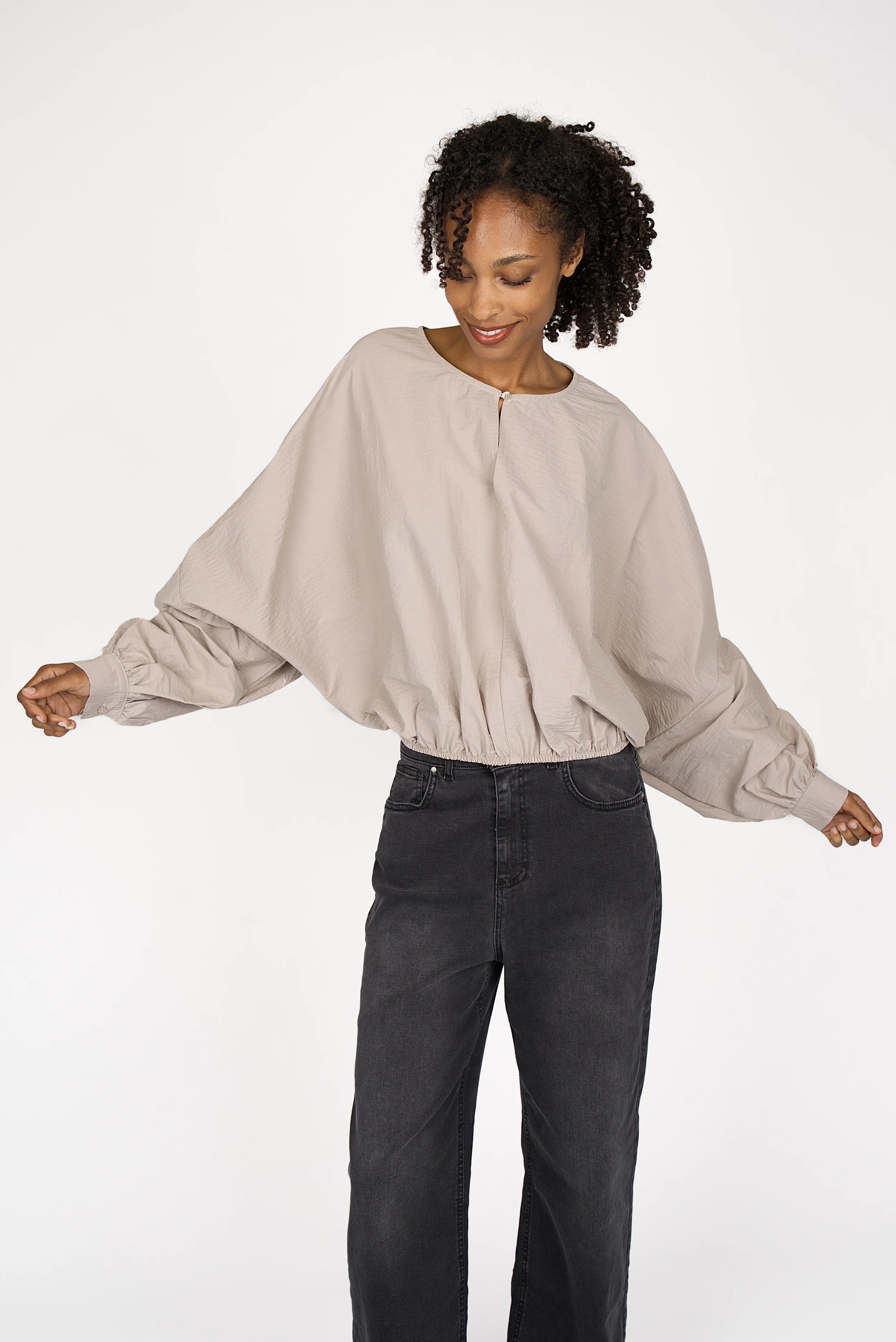 Woman wearing a loose fit MILLIE Crinkle Bluse with balloon sleeves and elastic hem in light beige paired with black pants.