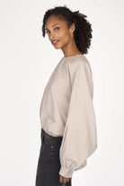 Woman wearing beige MILLIE Crinkle Bluse with sculptural balloon sleeves and elastic waistband in loose fit and cropped length