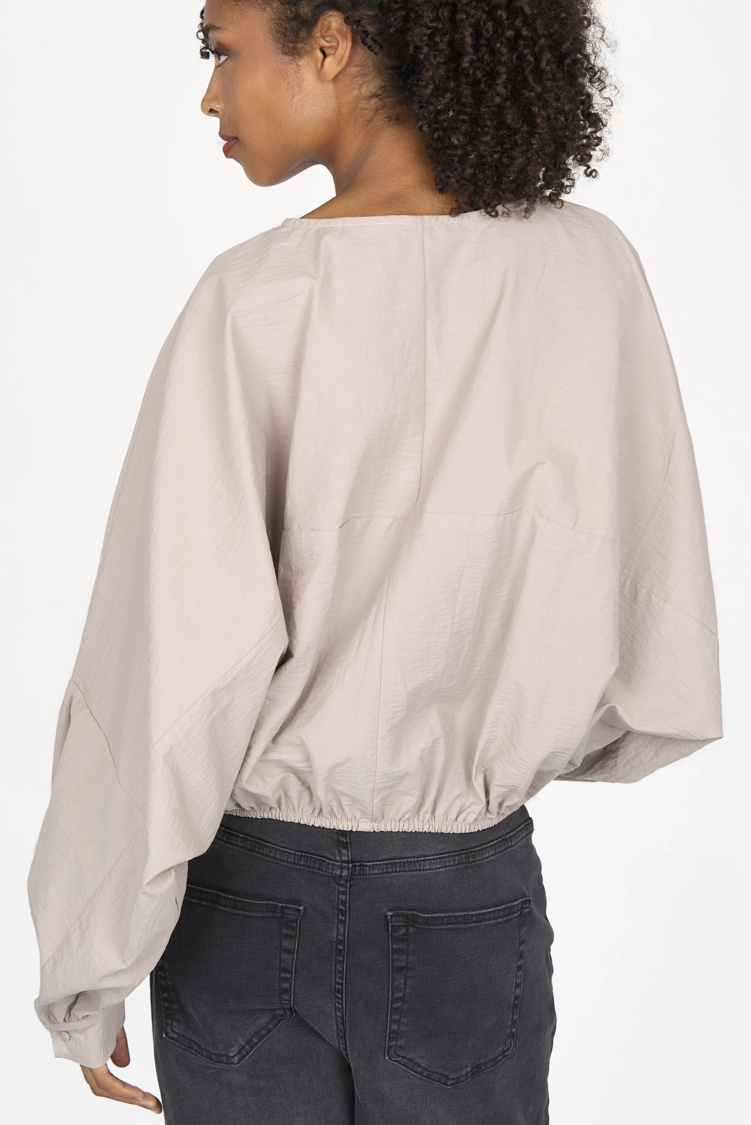 Back view of a woman wearing a loose fit MILLIE Crinkle Bluse with balloon sleeves and elastic hem in a light beige color