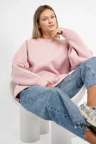 Woman wearing pink NAIRA Cozy Sweater with A-line fit and brushed cotton inside sitting on white chair