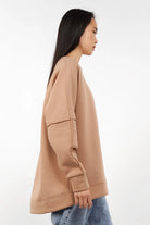 Side view of a woman wearing a beige NAIRA Cozy Sweater with A-line silhouette and brushed soft cotton fabric