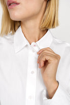 Close-up of a woman buttoning the collar of a white NATI Statement Oversize popelin shirt.
