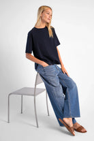 Damen trägt NITI.K Shirt aus hochwertiger Baumwolle mit kastiger Passform, Rundhalsausschnitt und seitlichen Schlitzen, kombiniert mit weitem Jeanshose und Sandalen.