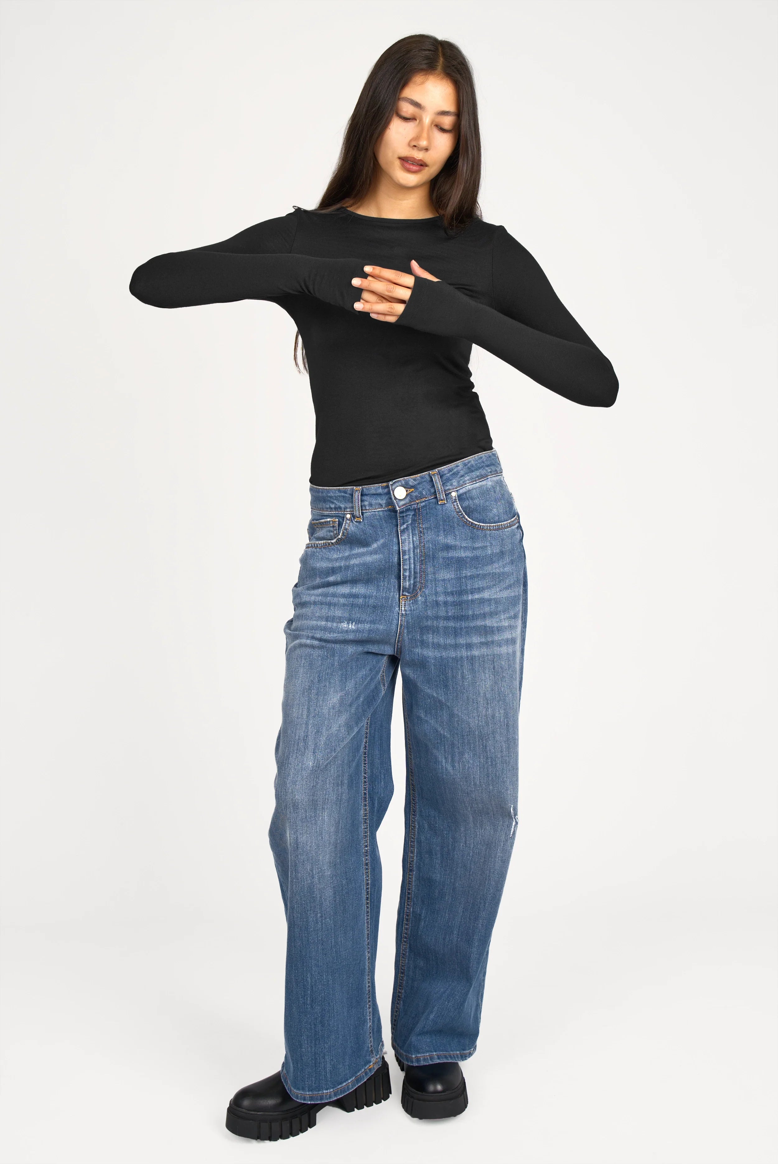 Woman wearing black NJELI Longsleeve with round neckline, extra-long sleeves with thumb holes, and slim fit paired with blue jeans