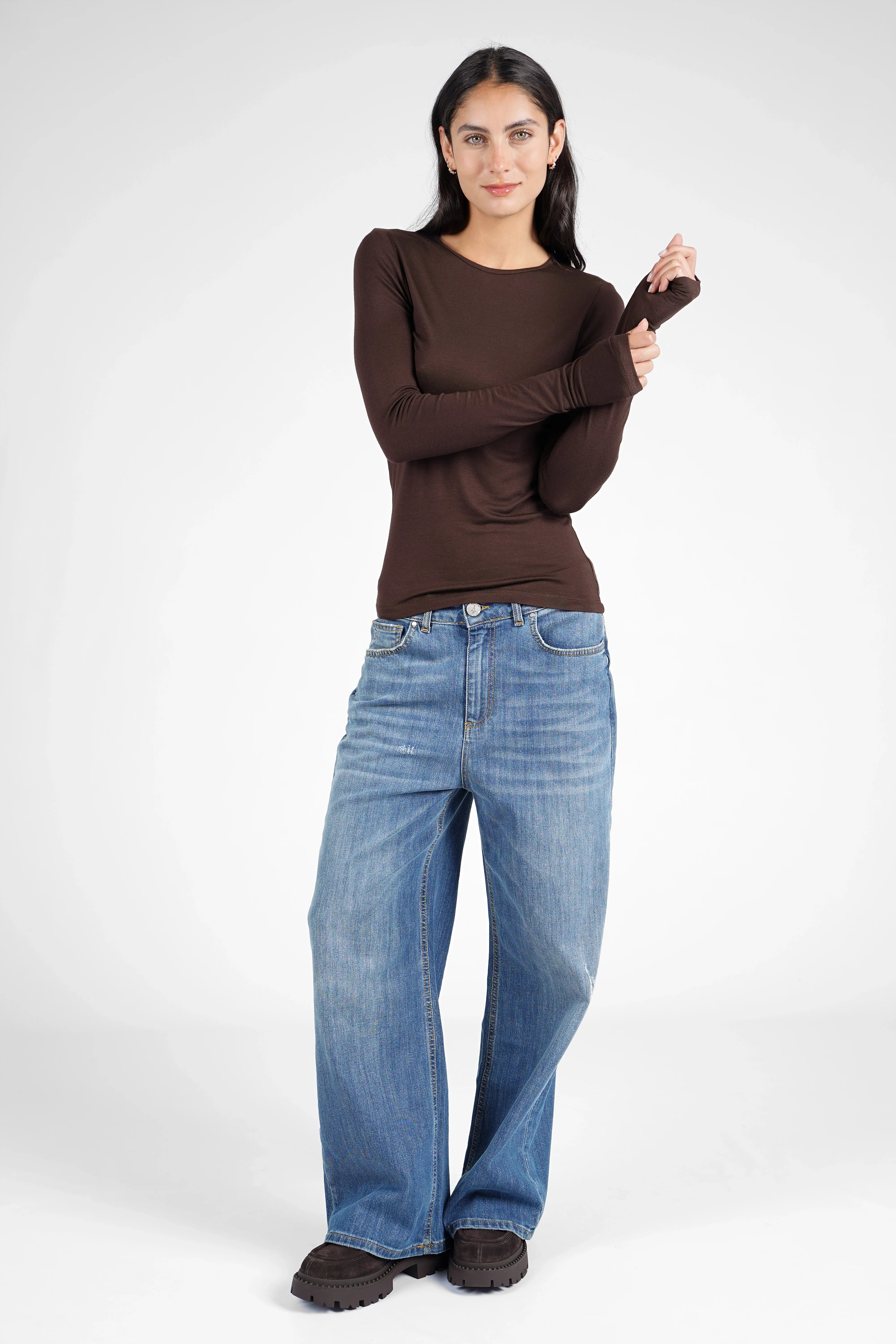Woman wearing a brown slim fit NJELI Longsleeve with round neckline and extra long sleeves with thumb holes paired with blue jeans