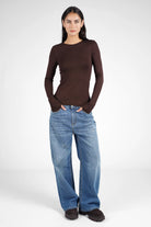 Woman wearing brown NJELI Longsleeve with round neckline, extra long sleeves with thumb holes, paired with blue wide-leg jeans