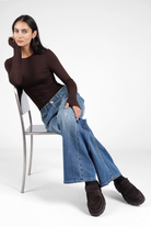 Woman wearing brown NJELI Longsleeve with round neckline, thumb holes, and slim fit paired with wide-leg jeans and black shoes sitting on a chair