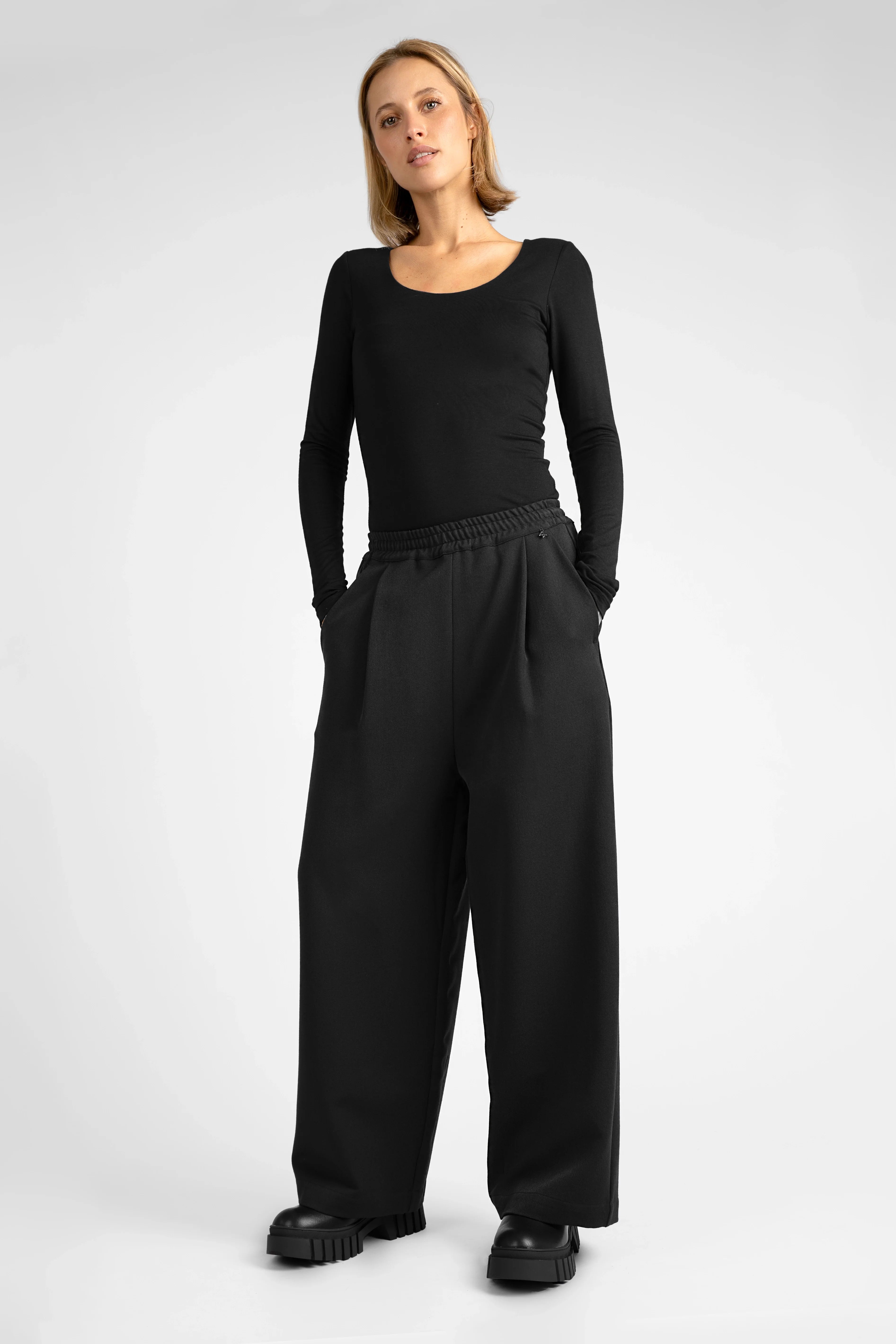 Frau trägt schwarze ONA Wide-Leg Hose mit elastischem Bund und seitlichen Taschen.
