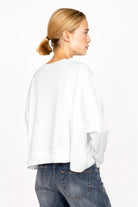 Weißes OSASU Cropped Longsleeve mit weitem Rundhalsausschnitt und lockerer Kastenform, vorne kürzer, hinten länger getragen.
