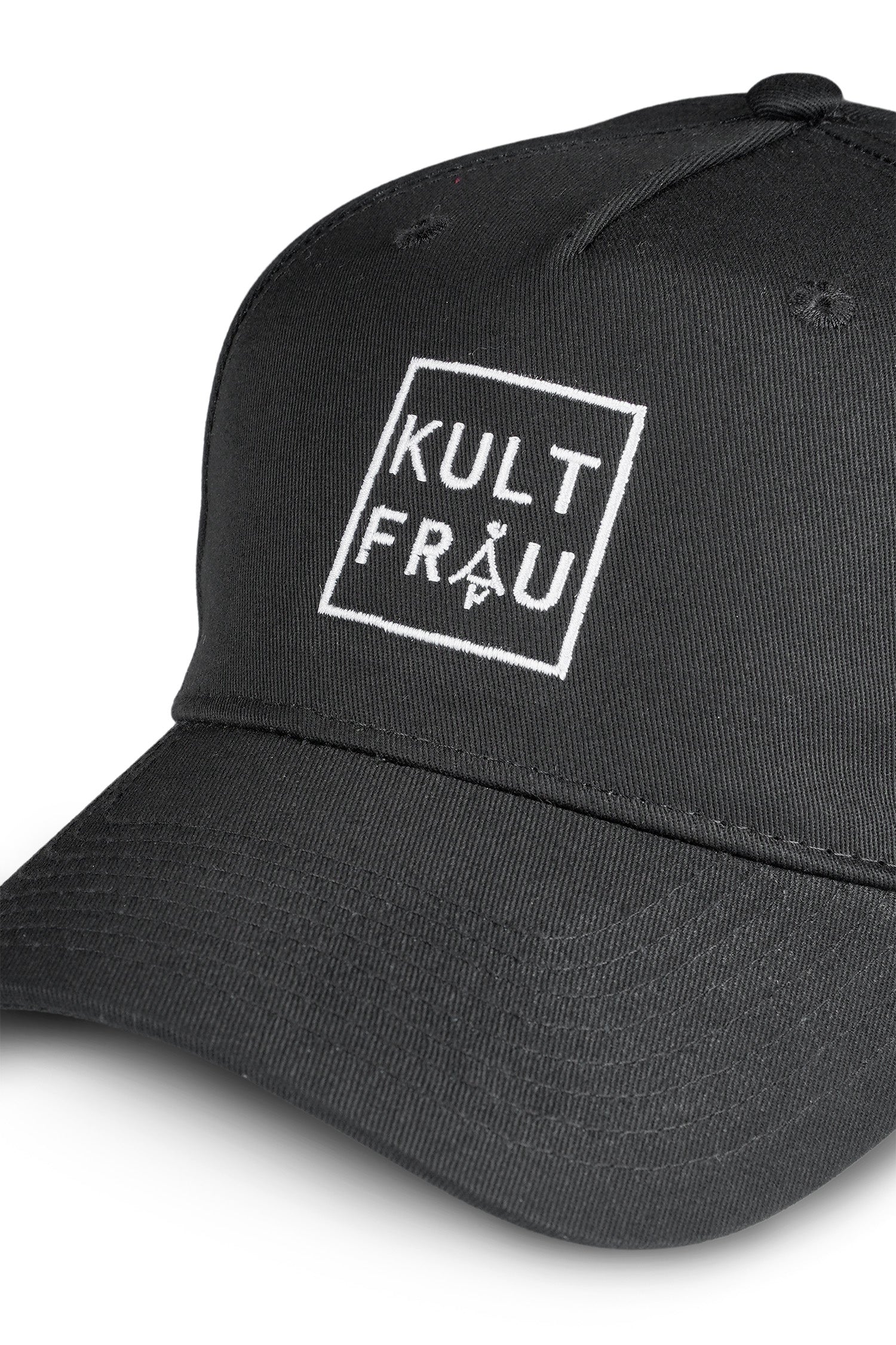 Eine Nahaufnahme einer schwarzen Cap aus glattem Material. Auf der Vorderseite ist ein auffälliger, weißer Logo-Stick zu sehen: Ein quadratischer Rahmen mit dem Brandnamen "KULTFRAU" in klaren Großbuchstaben. Der gebogene Schirm zeigt feine, parallel verlaufende Steppnähte. Die Struktur des Stoffes wirkt hochwertig und gleichmäßig, mit sauberen Nähten und minimalistischer Optik.