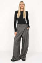Woman wearing RYONI Marlene-Hose high-waist wide-leg grey trousers with asymmetrical buttoned waistband and side pockets.