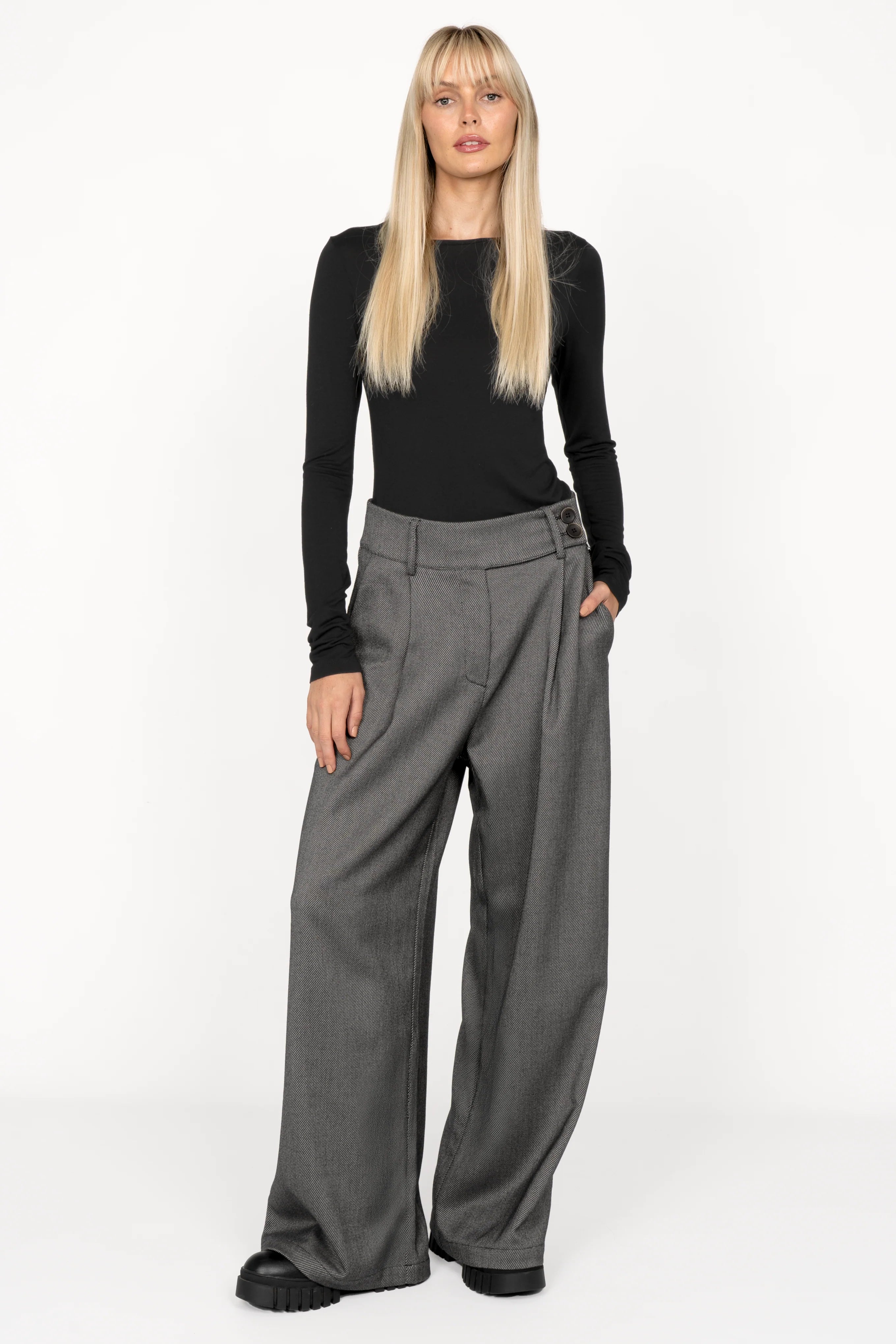 Woman wearing RYONI Marlene-Hose high-waist wide-leg grey trousers with asymmetrical buttoned waistband and side pockets.