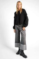 Woman wearing black SEATA Cropped Sweater with oversized fit, round neckline, drawstring waistband, and elastic cuffs paired with wide-leg jeans and black boots