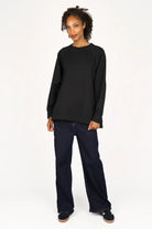 Woman wearing black SELKA Sweater with A-line shape, raglan sleeves, wide cuffs, and longer back hem, paired with dark jeans.