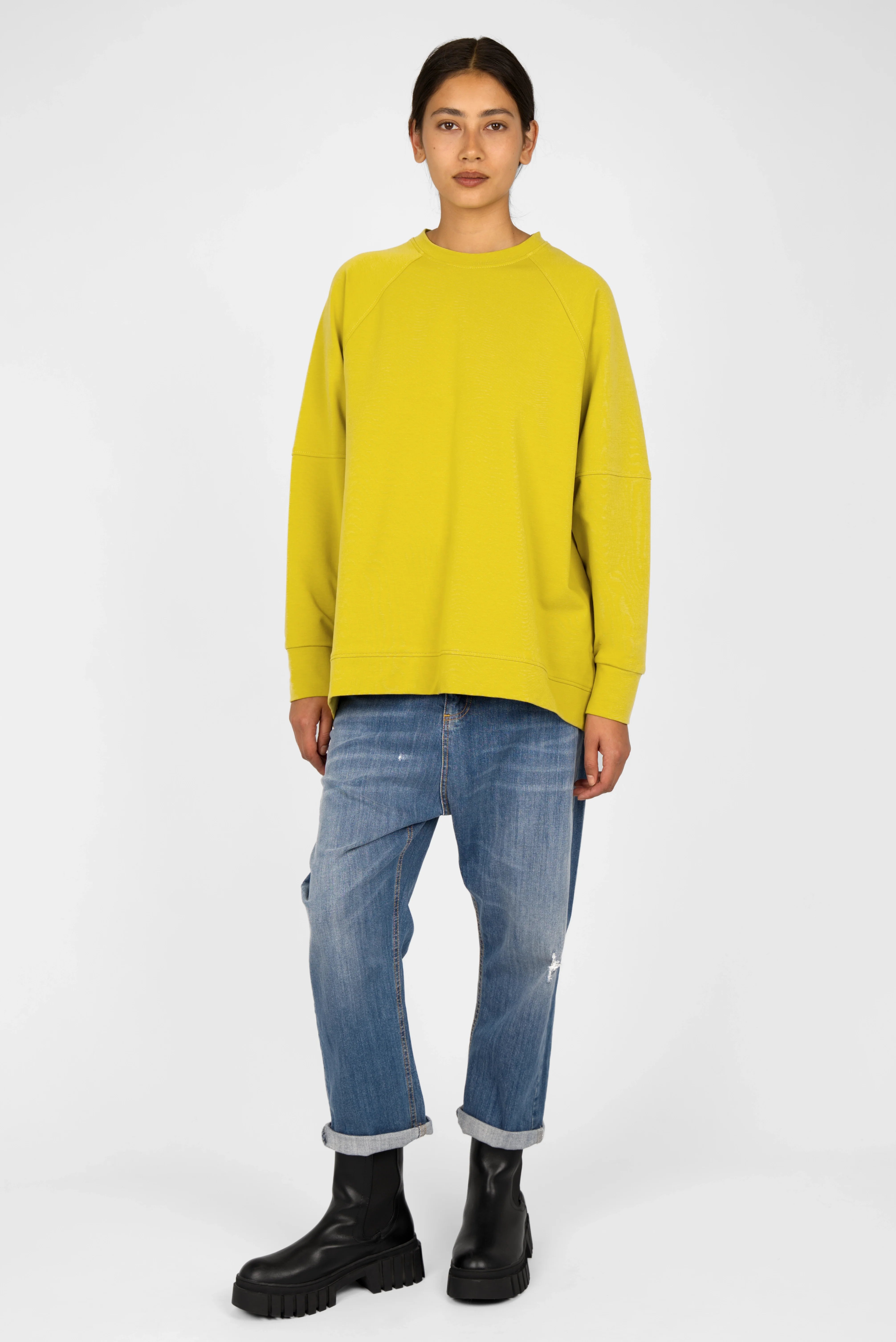 Yellow SELKA Sweater with A-line relaxed fit, raglan sleeves, rounded hem longer at the back, and tonal logo embroidery worn with blue jeans and black boots.