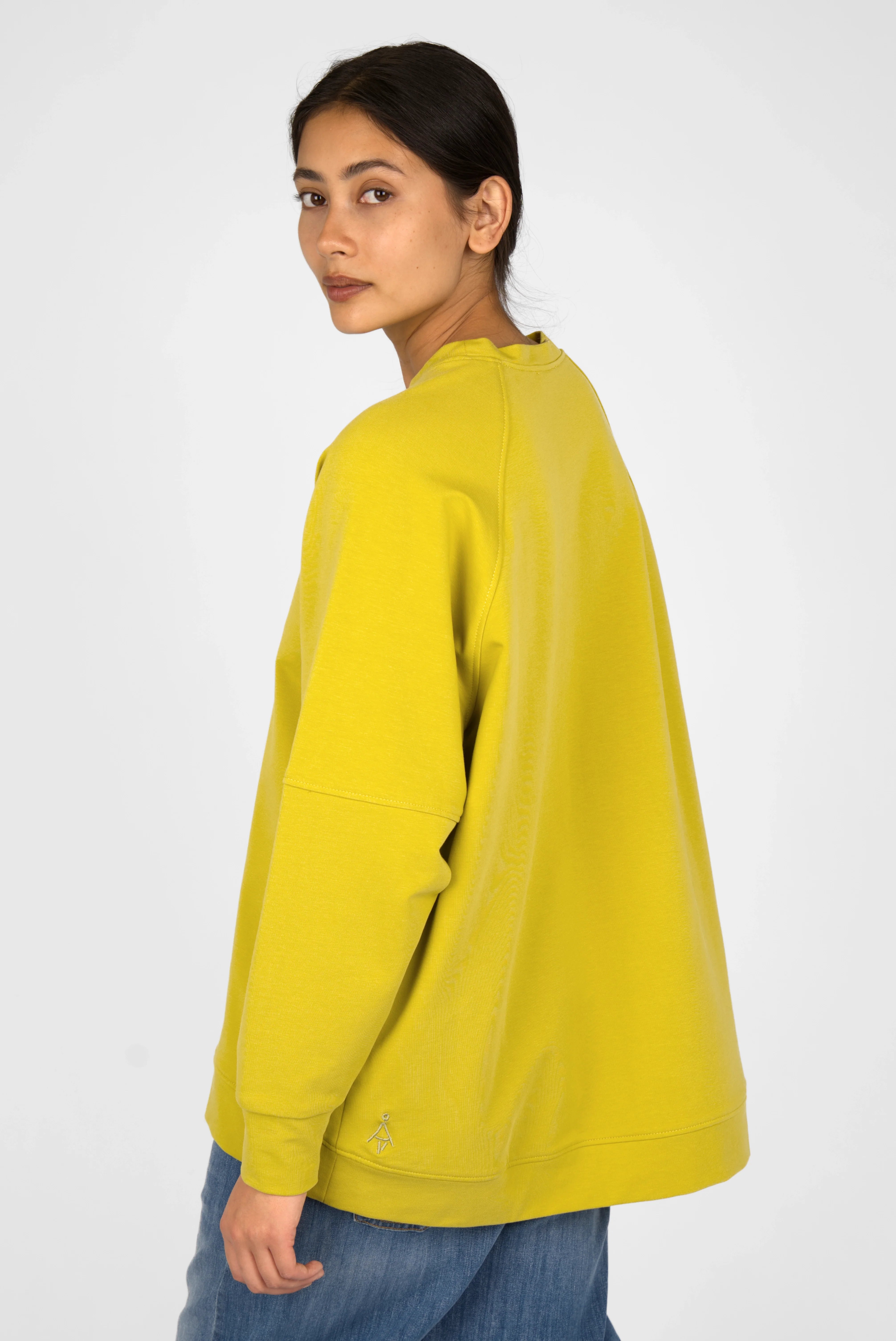 Woman wearing yellow SELKA Sweater with A-line, raglan sleeves, and longer back hem.