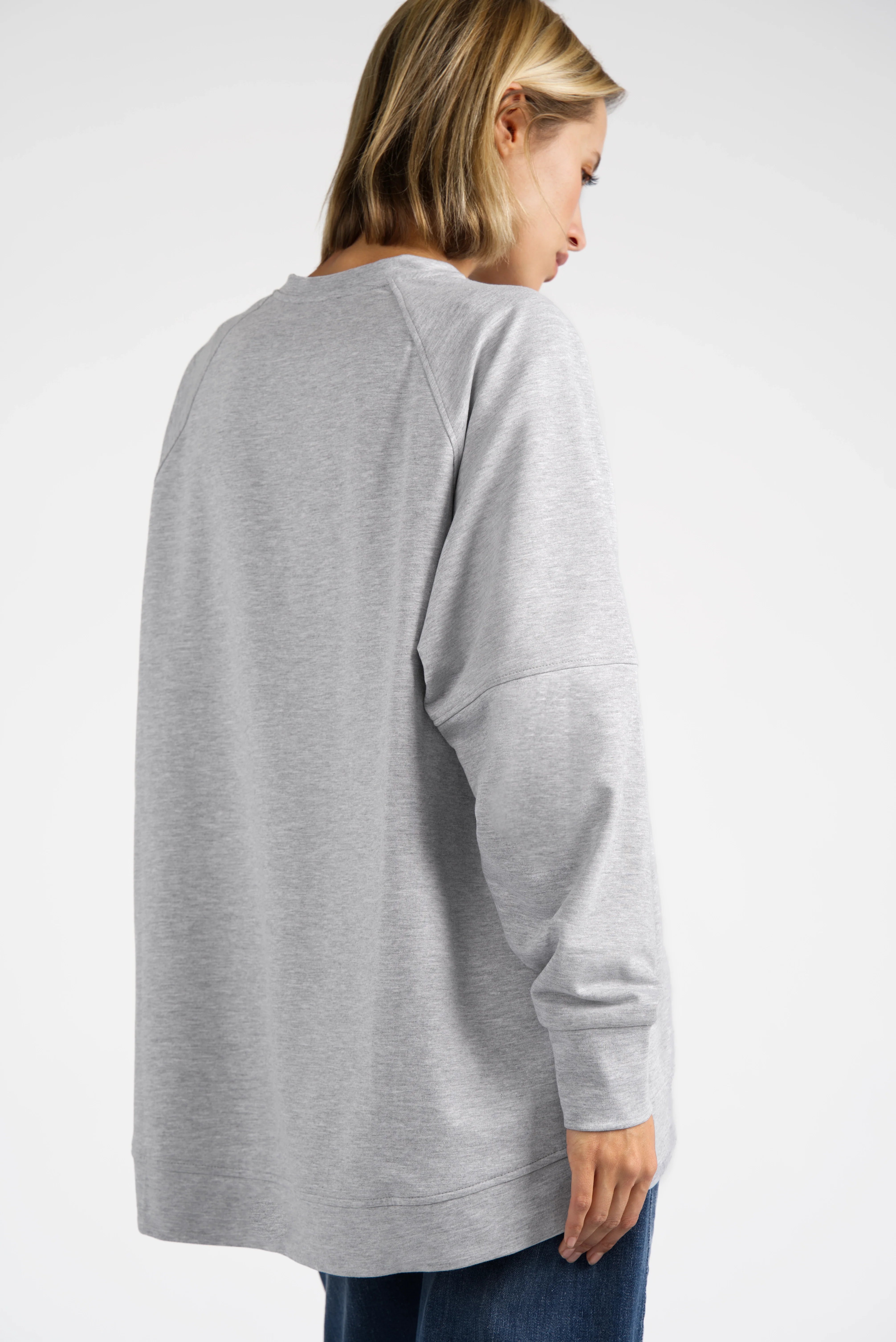 Back view of a woman wearing a relaxed fit grey SELKA Sweater with raglan sleeves and a longer back hem