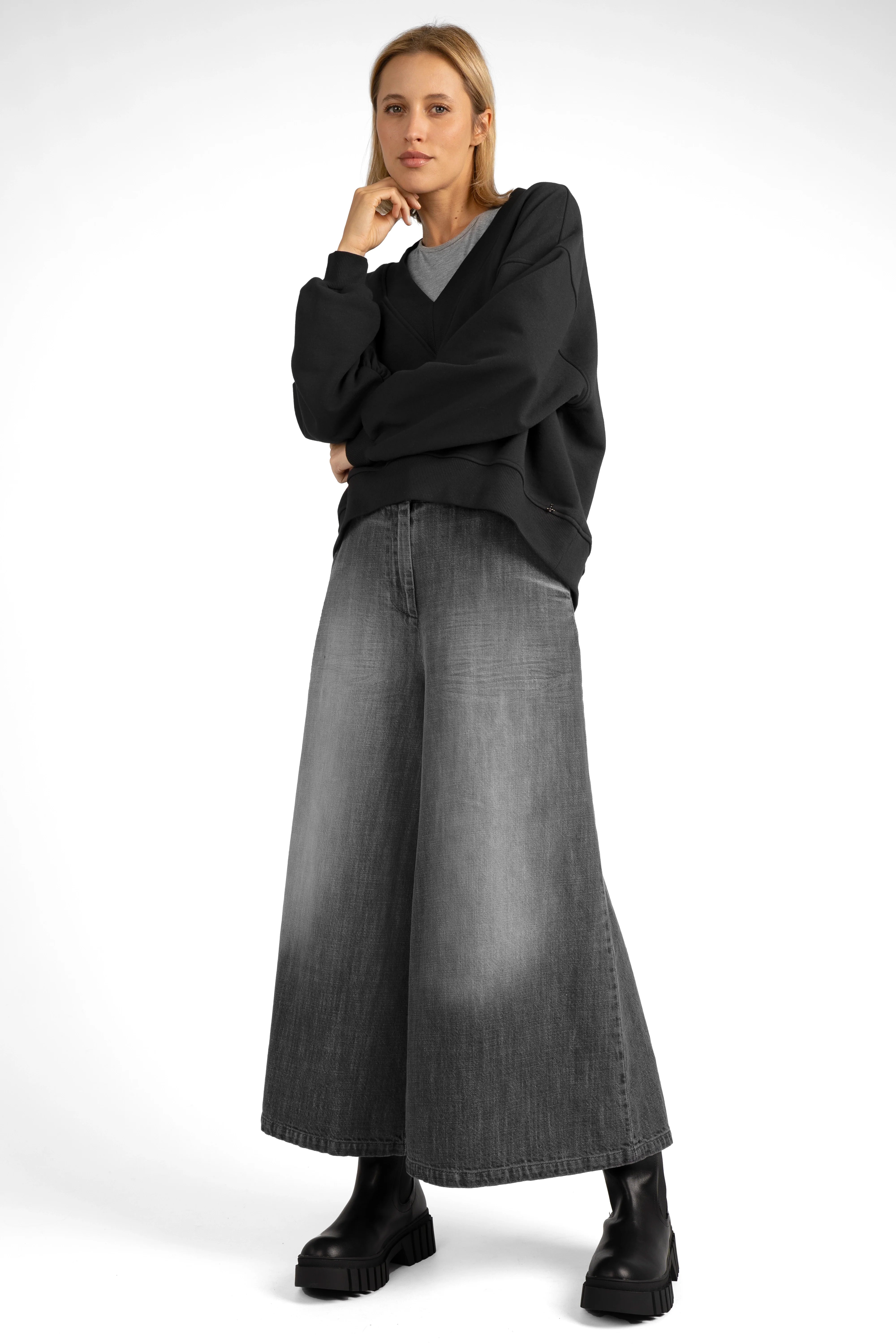 Woman wearing black SEREA Sweater mit V-Ausschnitt with deep V-neck, cropped hem, and gathered sleeve detail paired with wide-leg gray jeans and black boots.
